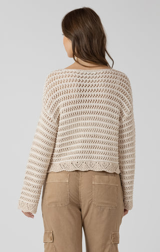Woman wearing a beige crochet sweater and brown pants on a plain background