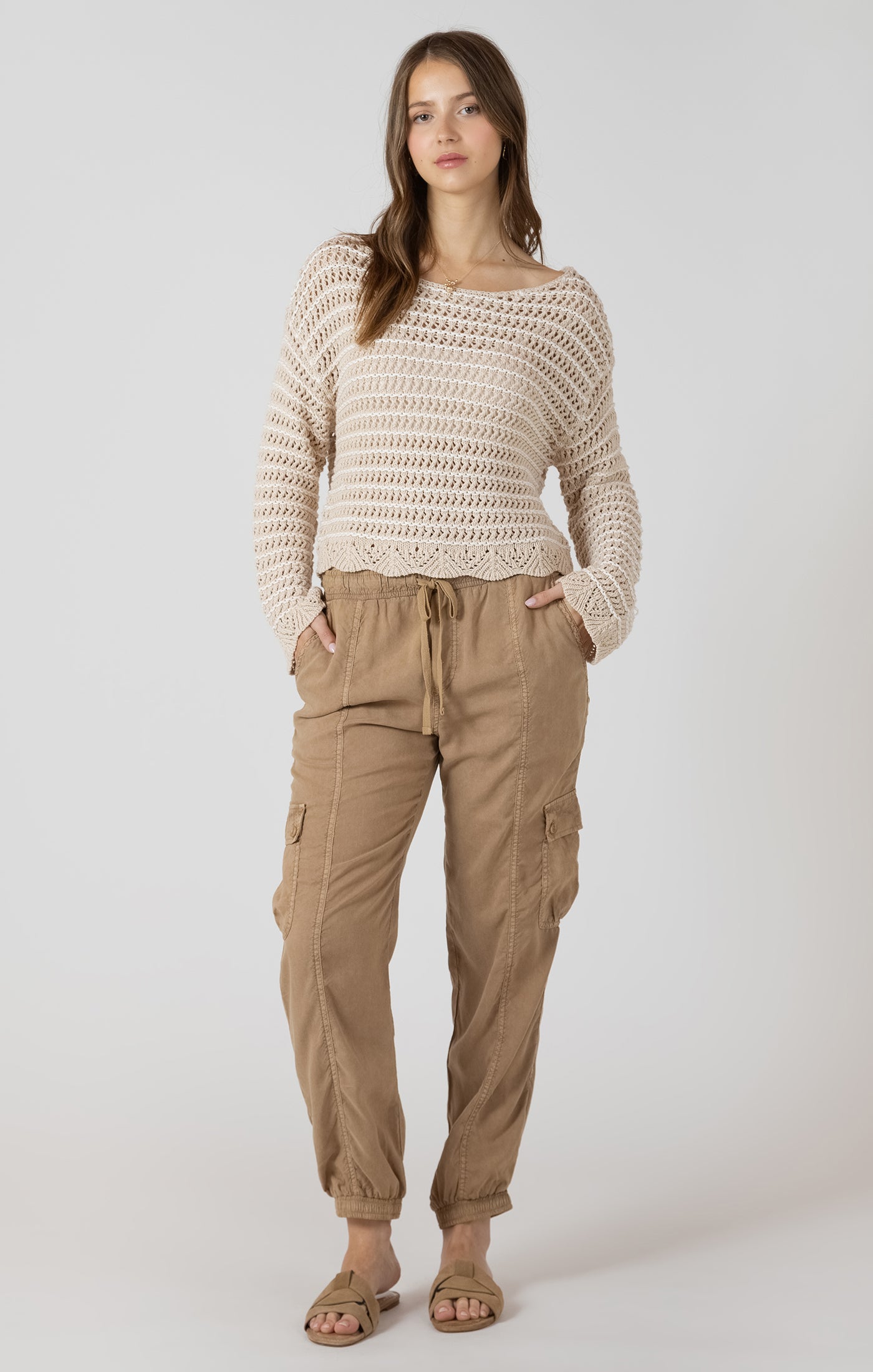 Woman wearing a beige crochet sweater and tan cargo pants on a white background