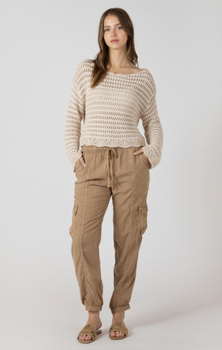 Woman wearing a beige crochet sweater and tan cargo pants on a white background