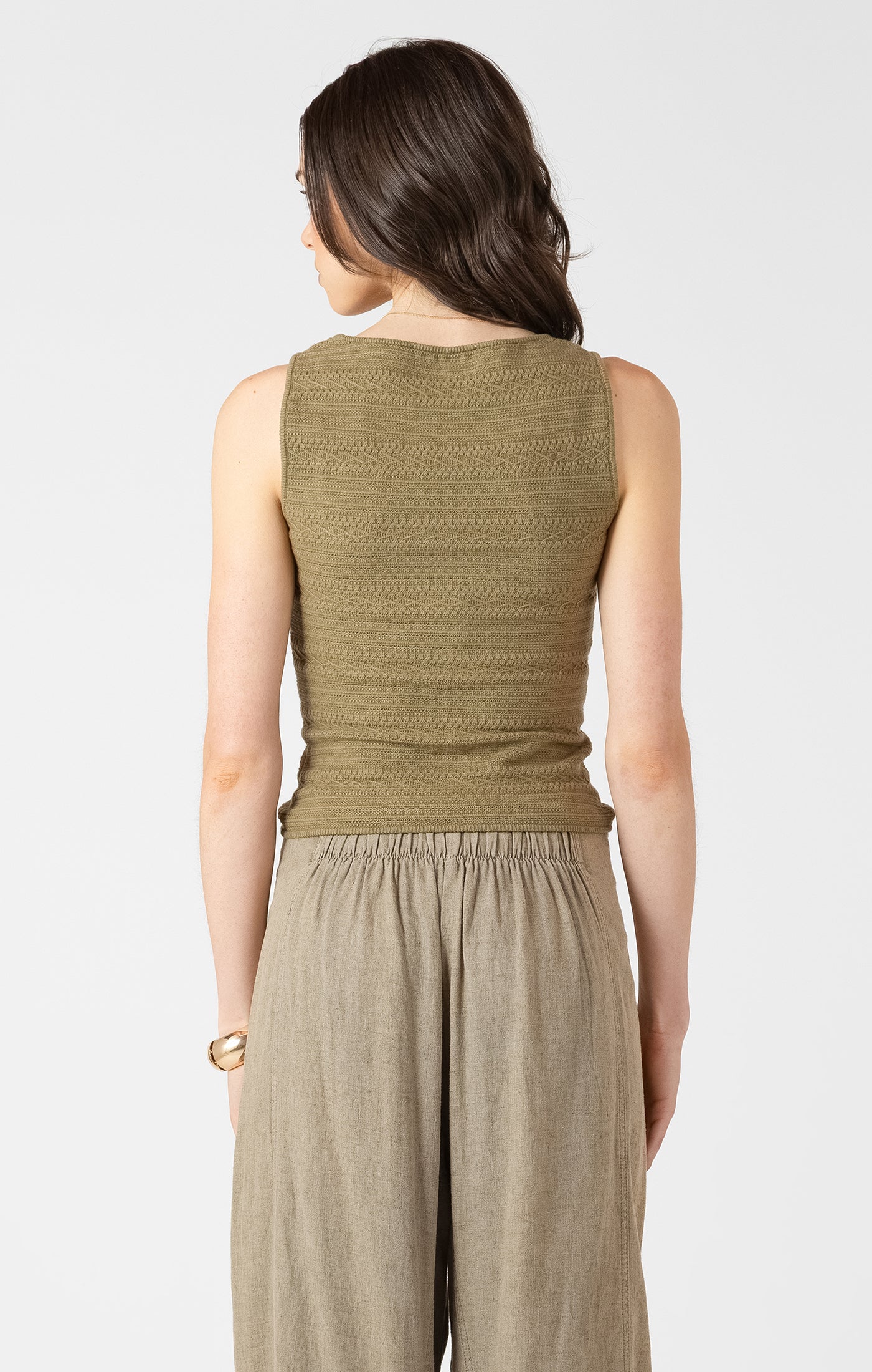 Woman wearing a green sleeveless top and beige pants on a white background