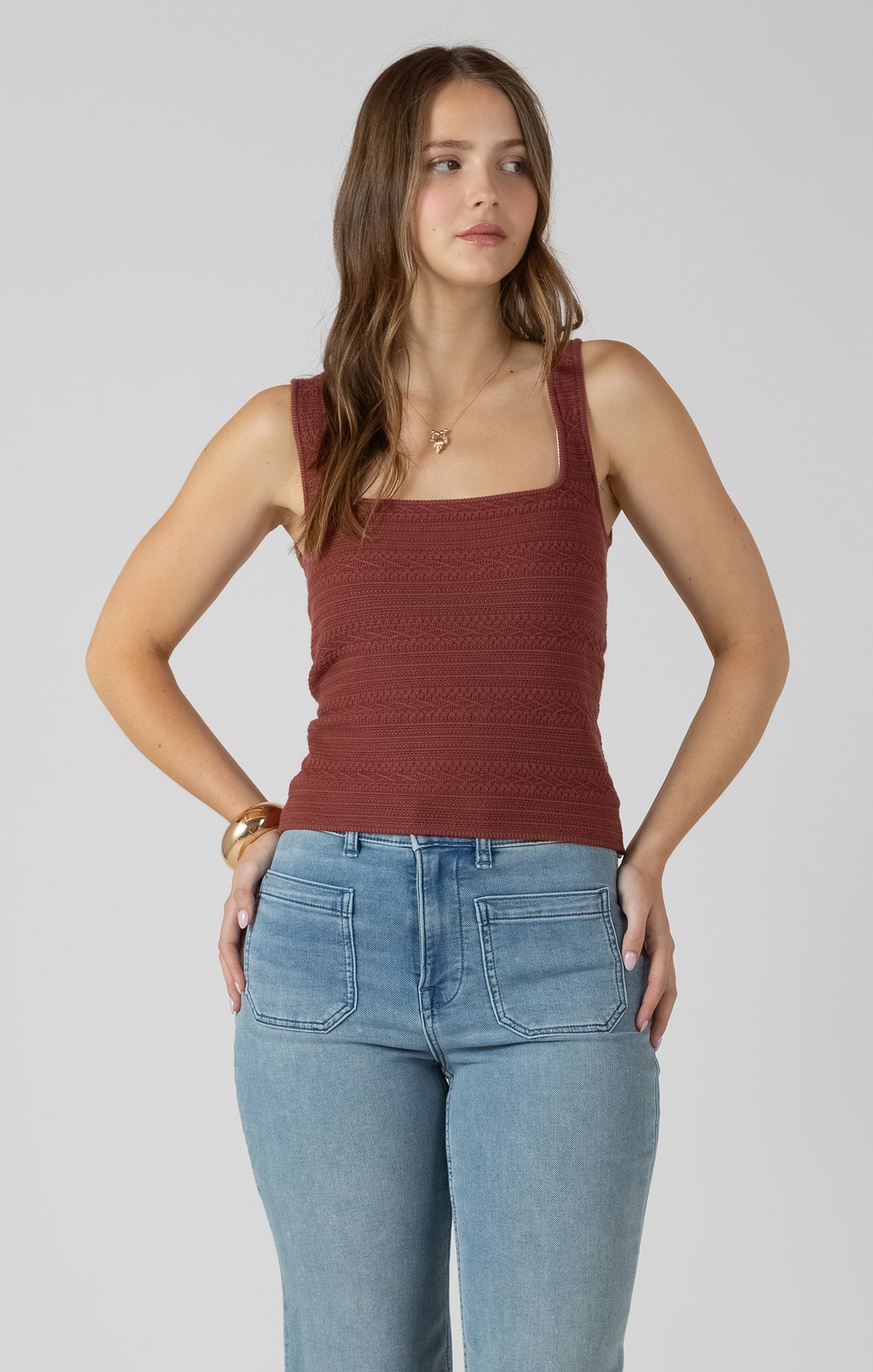 Woman wearing a rust-colored tank top and light blue jeans on a plain background