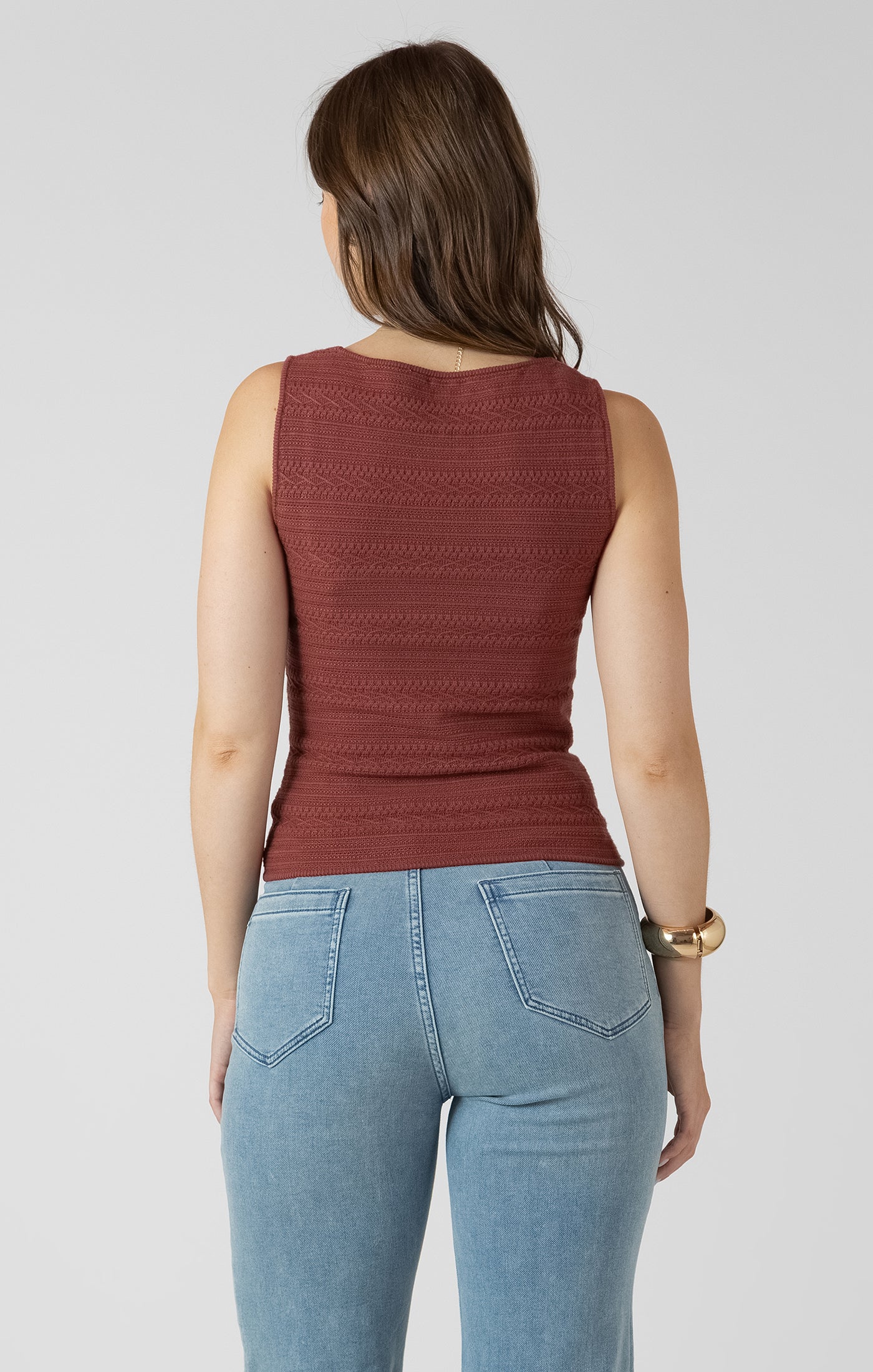 Woman wearing a rust-colored sleeveless top and light blue jeans on a plain background