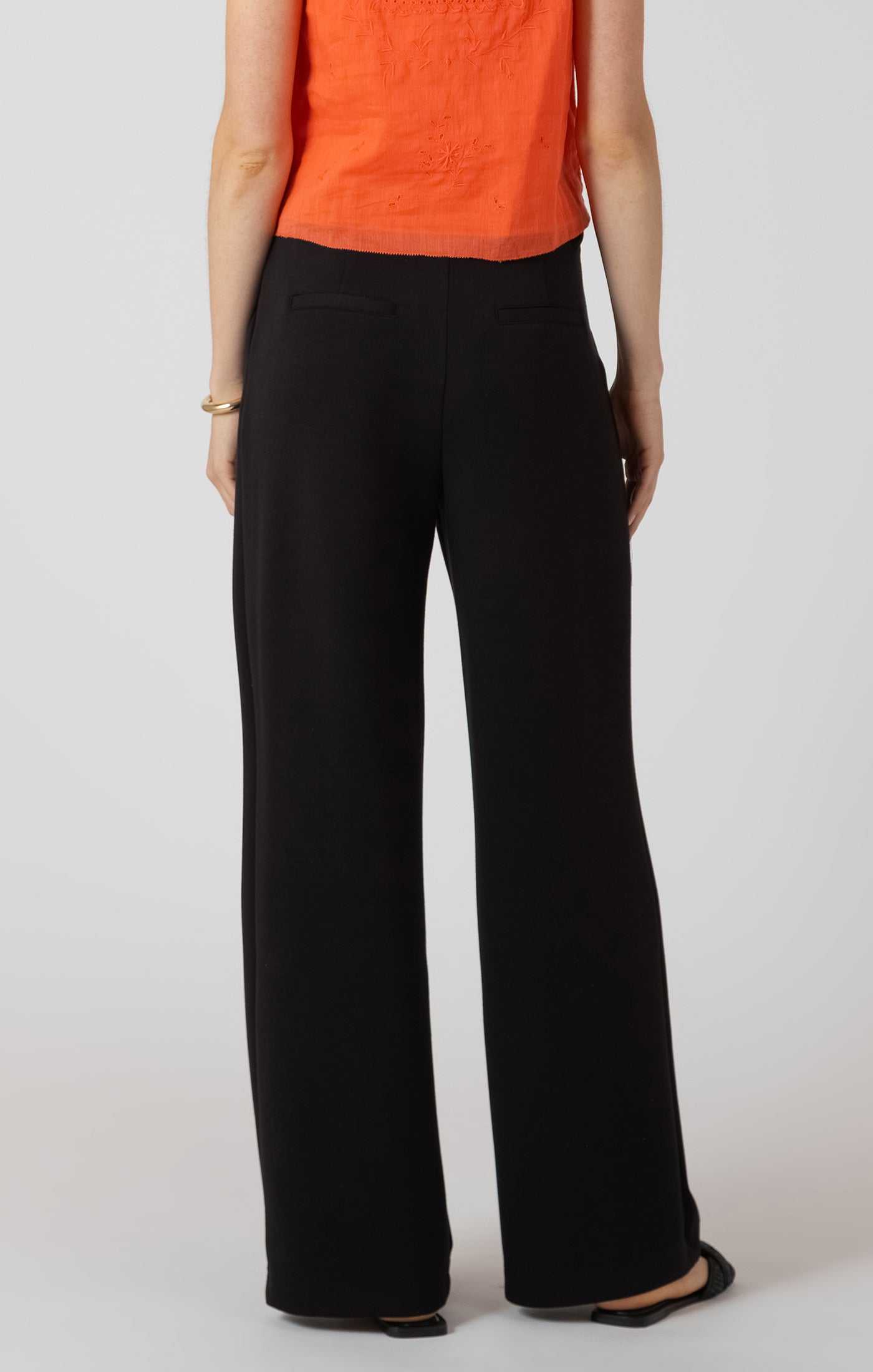 Person wearing black wide-leg pants and an orange top on a white background