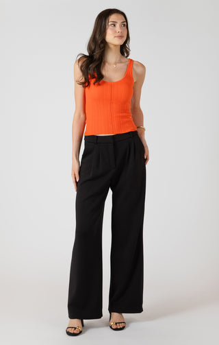 Woman wearing an orange top and black pants on a white background