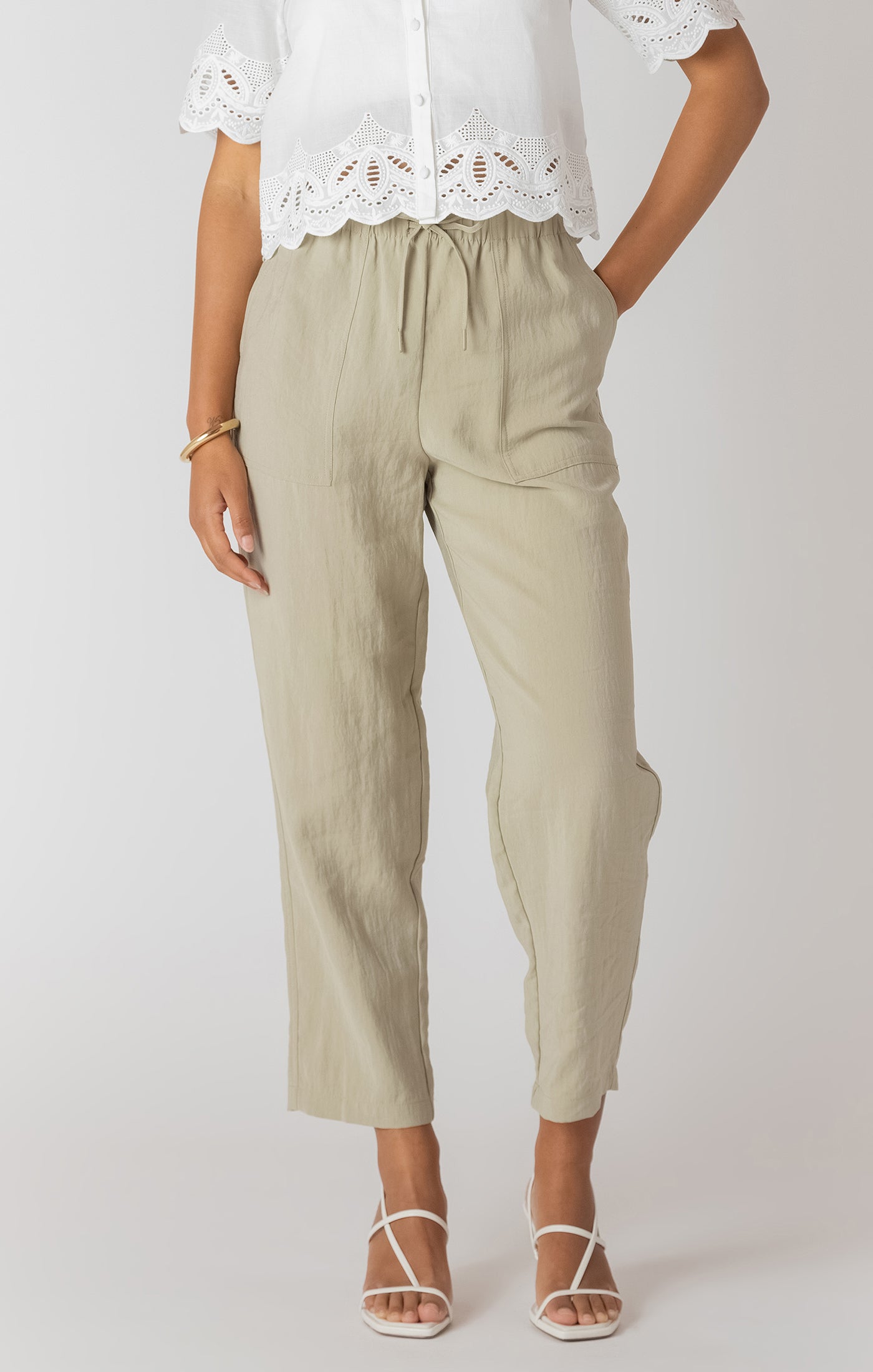 Person wearing beige pants and a white lace top on a plain background