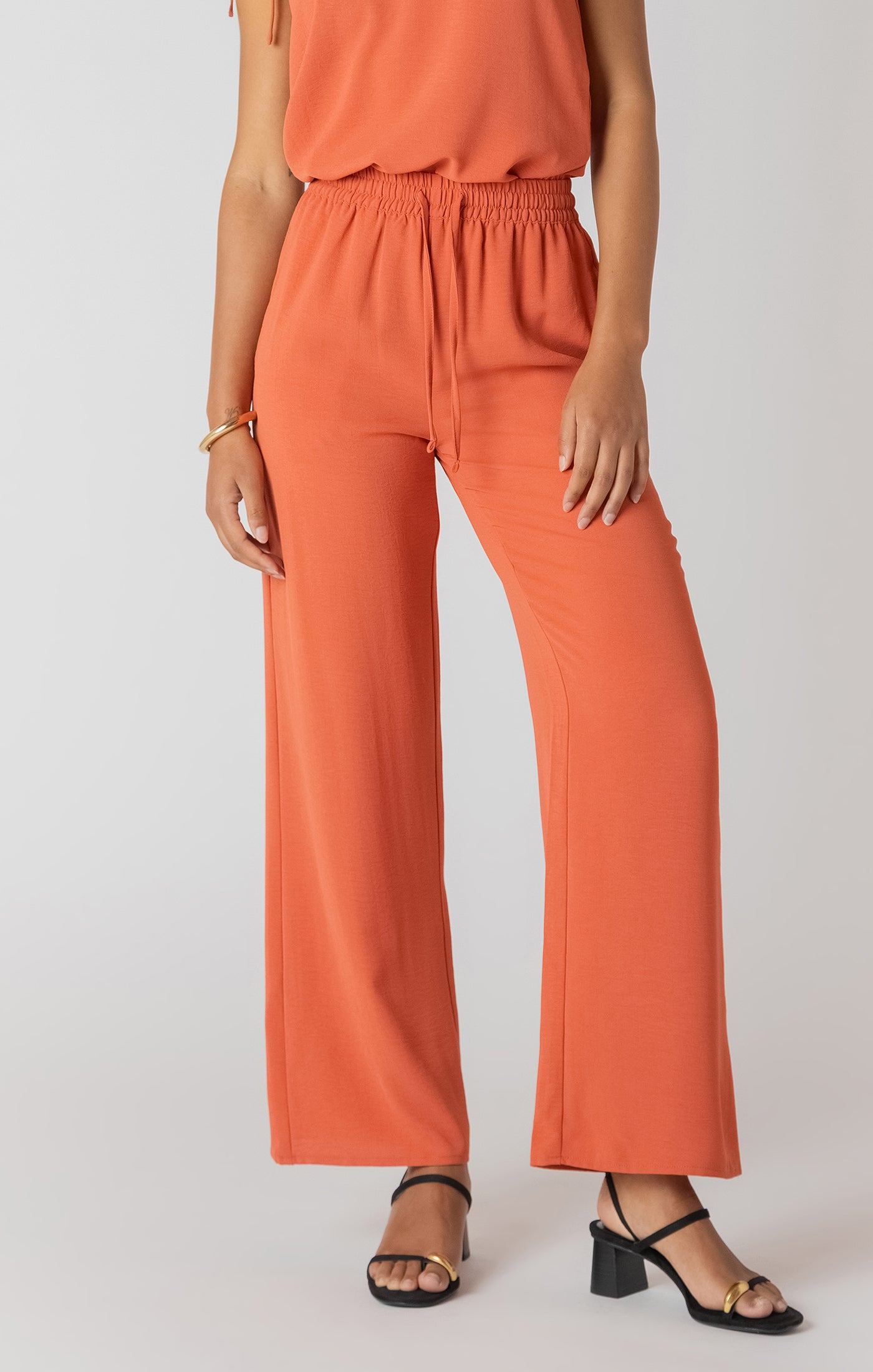 Person wearing orange pants and a sleeveless top on a plain background