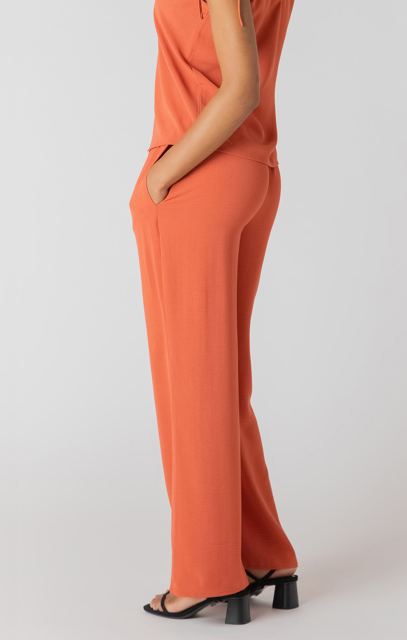 Person wearing an orange outfit with wide-leg pants on a white background