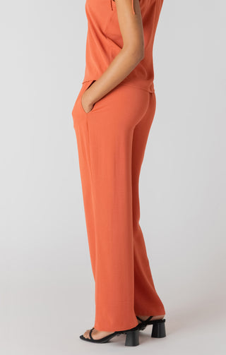 Person wearing an orange outfit with wide-leg pants on a white background
