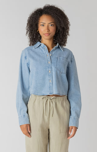 Woman wearing a light blue denim shirt and beige pants against a plain background