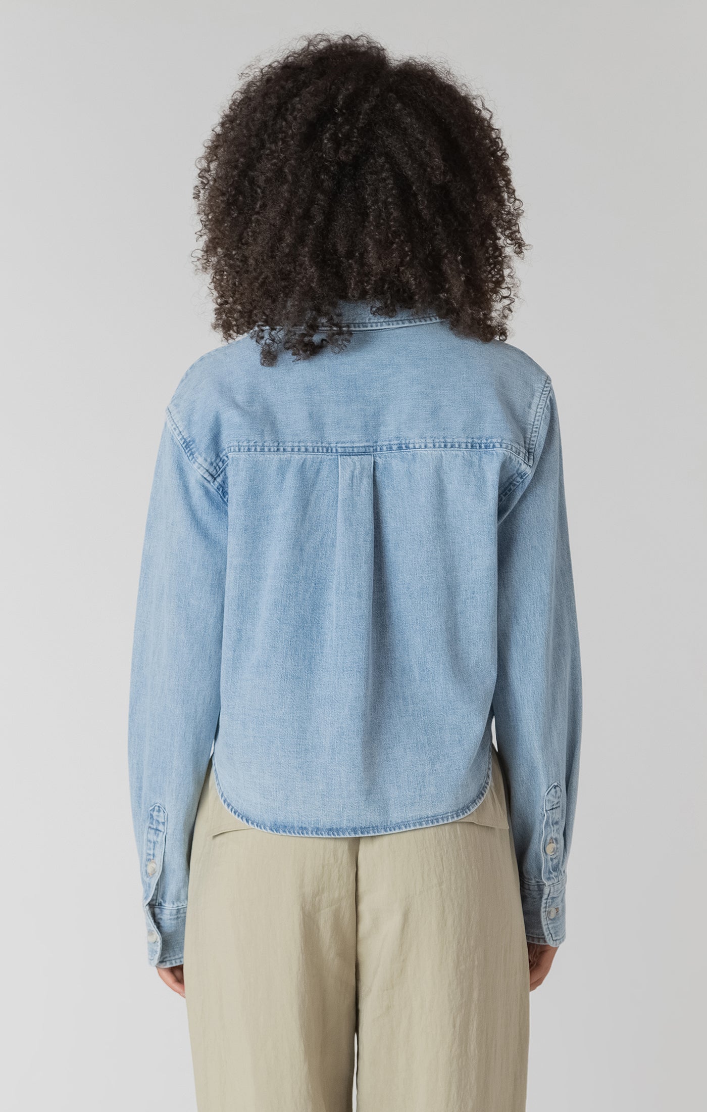 Person wearing a light blue denim shirt from behind on a plain background