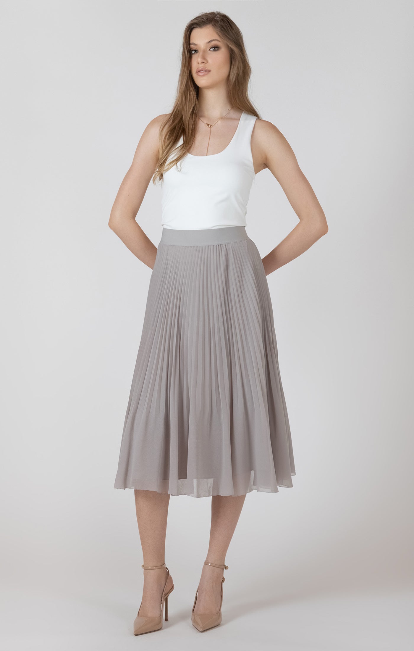 Woman wearing a white top and gray pleated skirt on a plain background