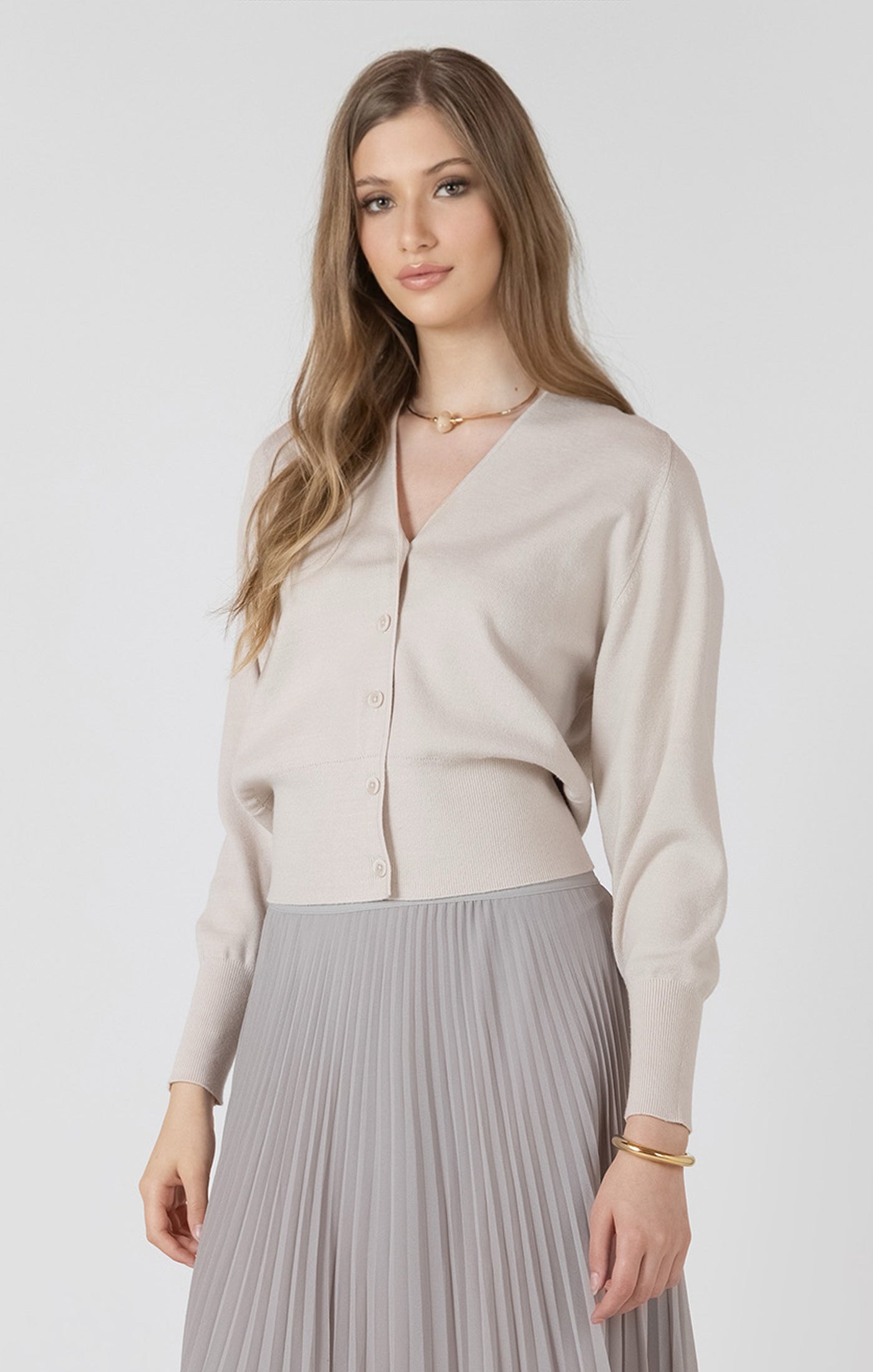 Woman wearing a beige cardigan and gray pleated skirt on a white background