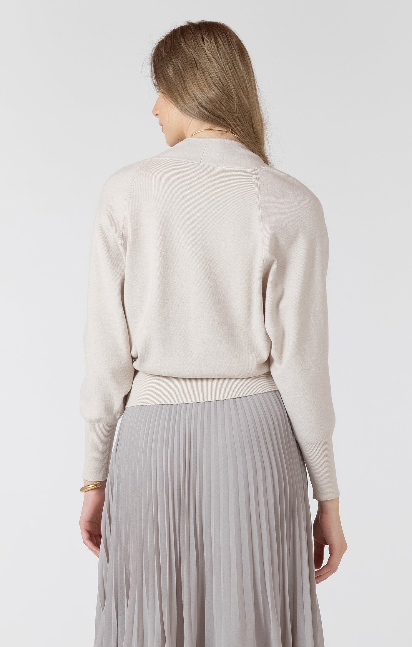 Woman wearing a light-colored sweater and pleated skirt on a plain background