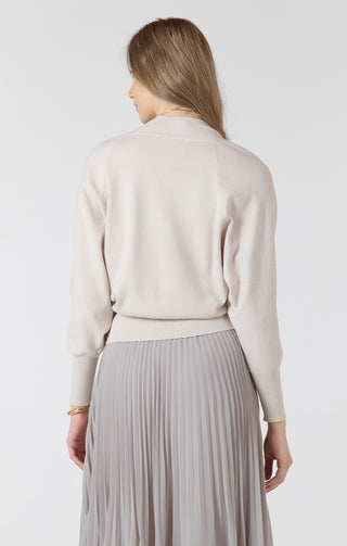 Woman wearing a light-colored sweater and pleated skirt on a plain background