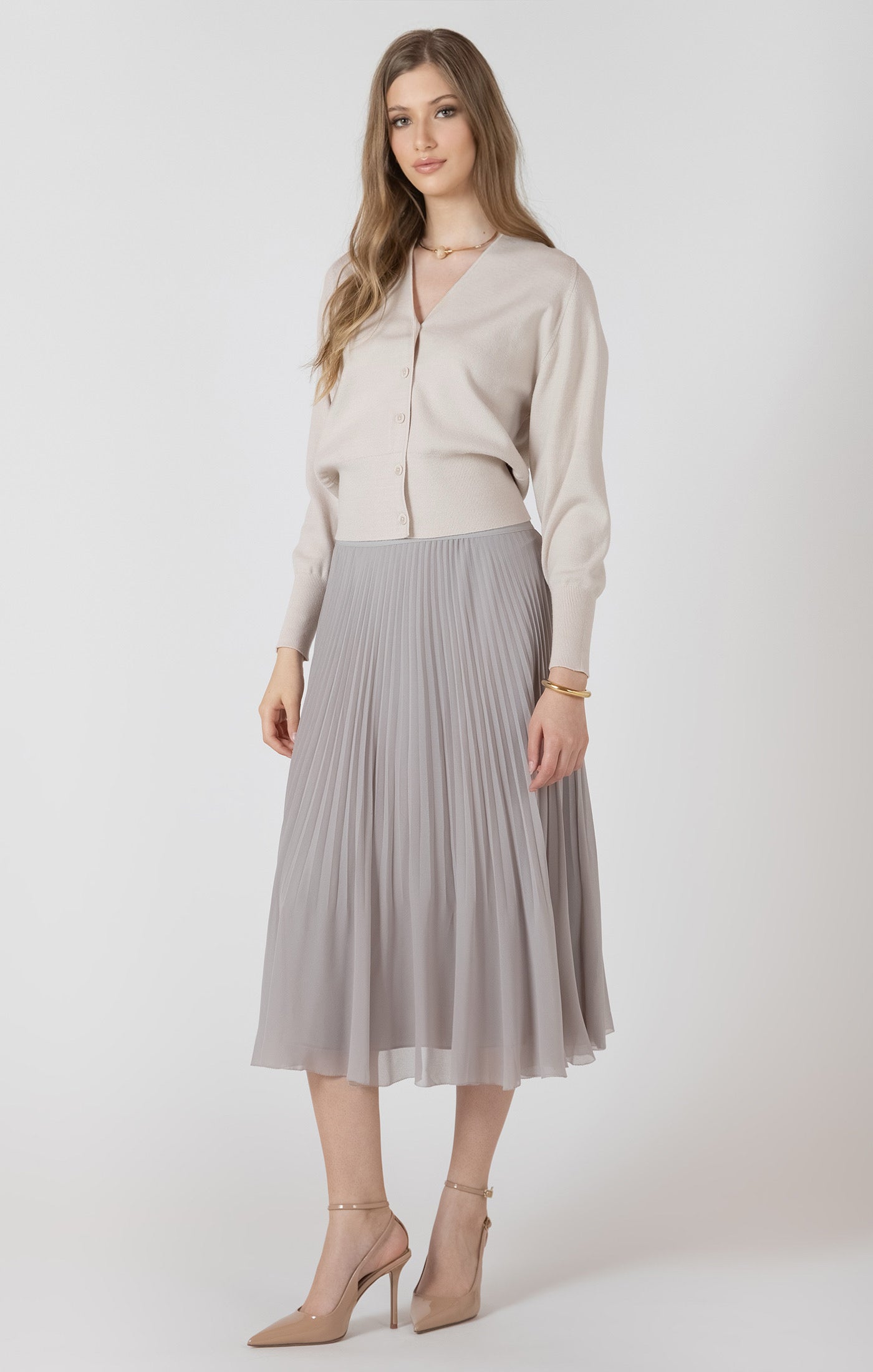 Woman wearing a light blouse and gray pleated skirt on a white background