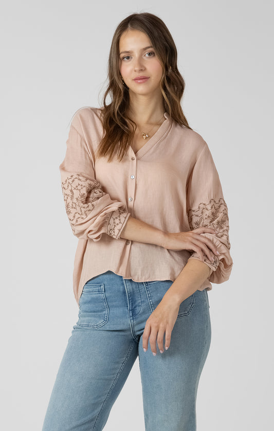 Woman wearing a light pink blouse with lace sleeves and blue jeans on a white background