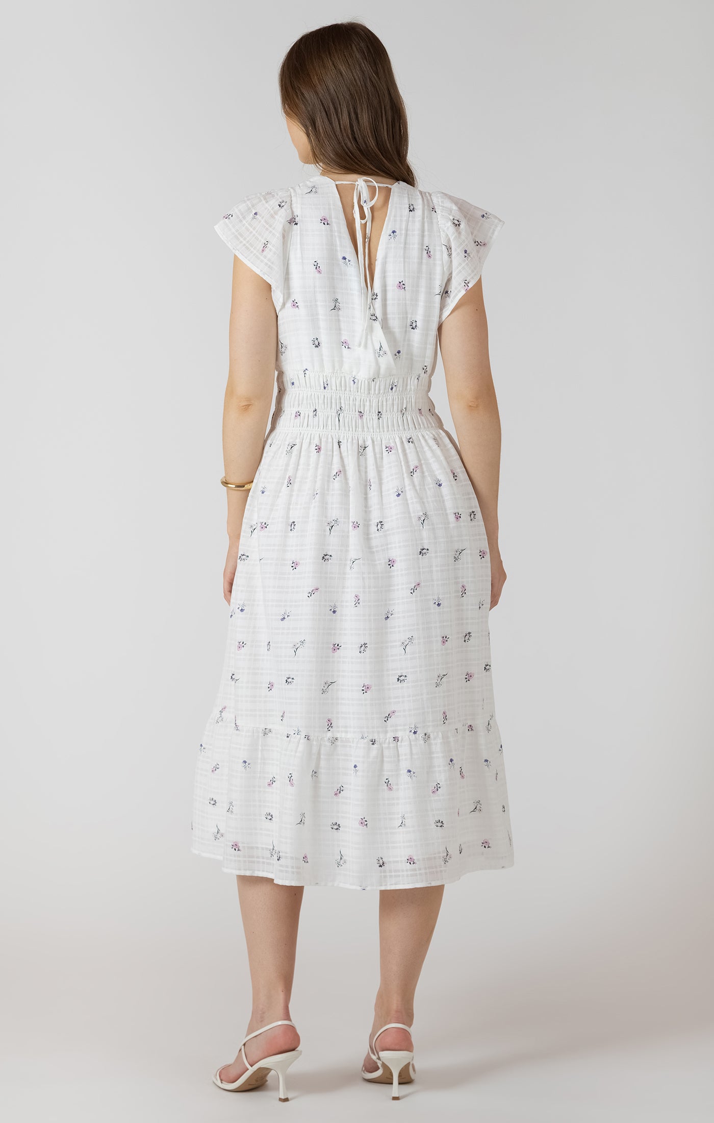 Woman wearing a white dress with a subtle pattern on a plain background