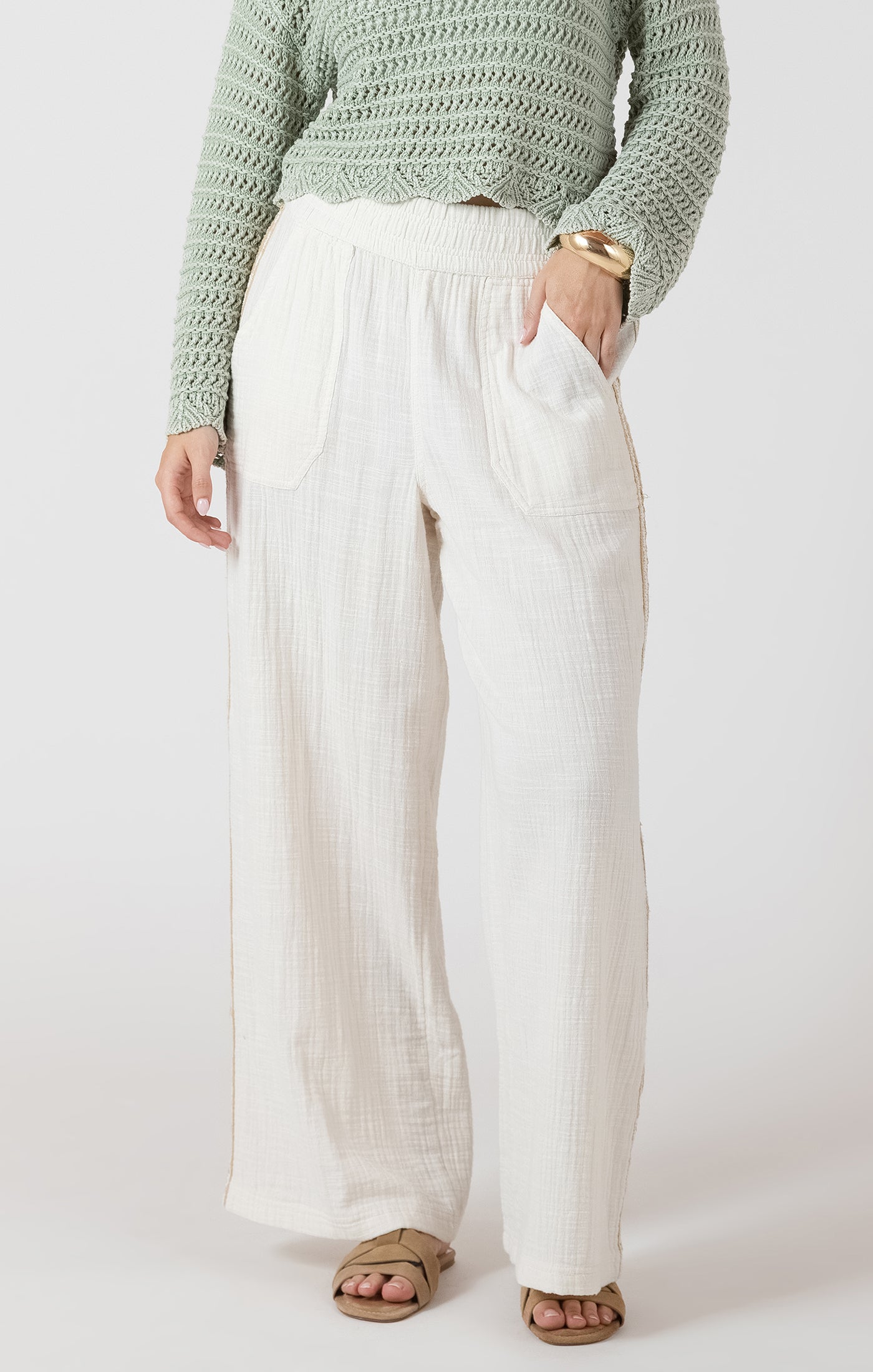 Person wearing a green sweater and white pants on a plain background