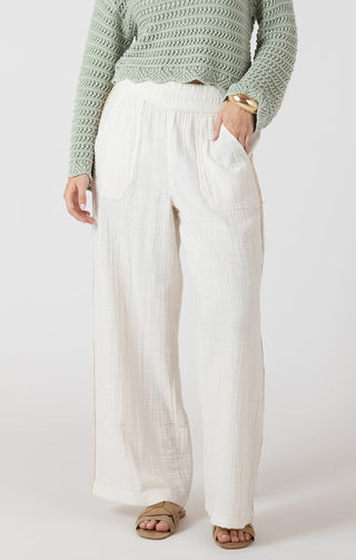 Person wearing a green sweater and white pants on a plain background