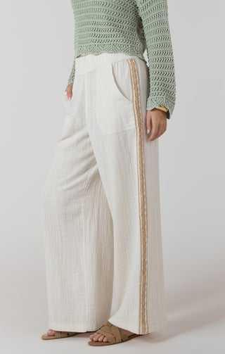 Person wearing a green knitted sweater and white pants with a gold stripe on a plain background