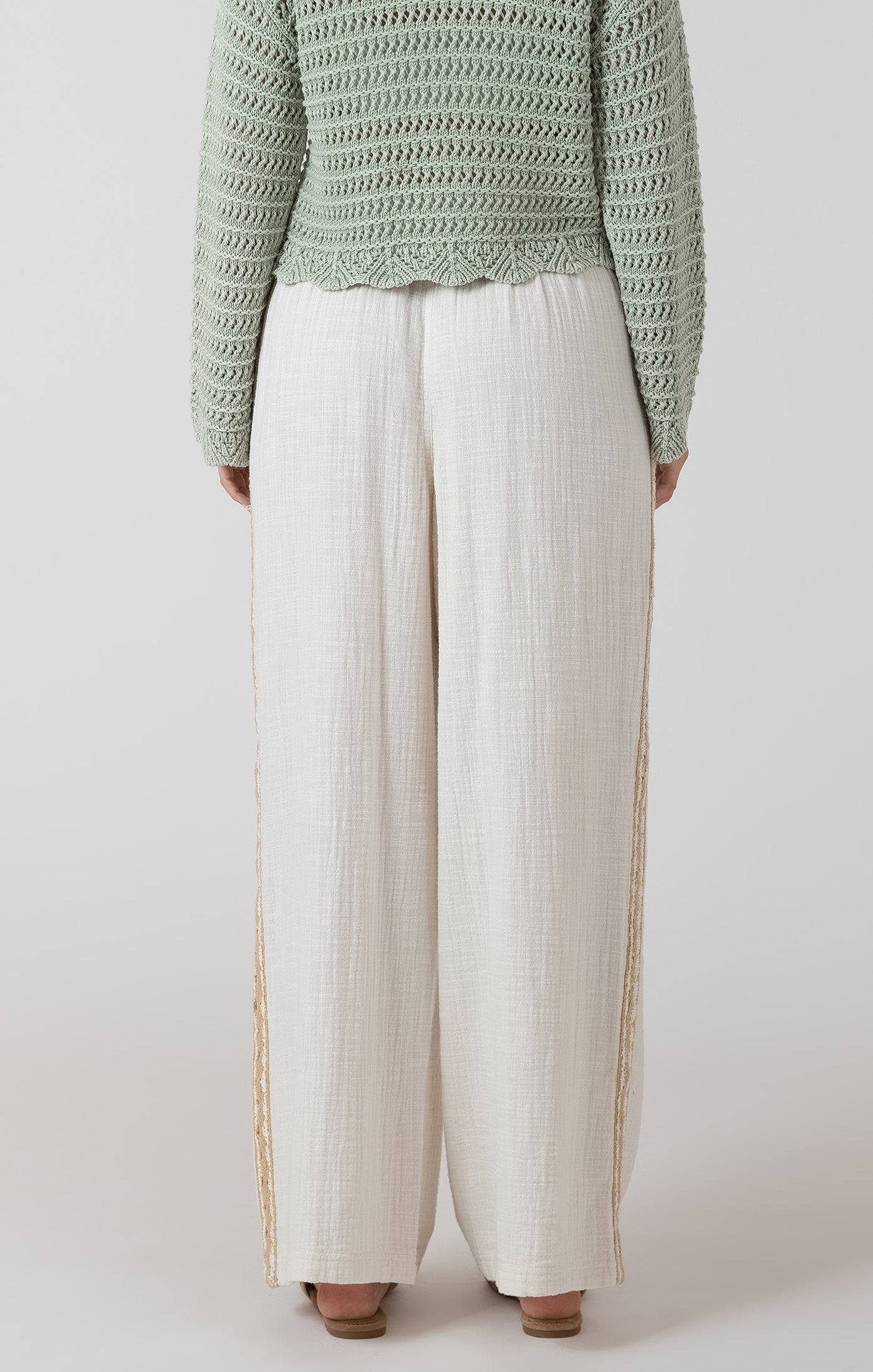 Person wearing a green textured sweater and white pants on a light gray background