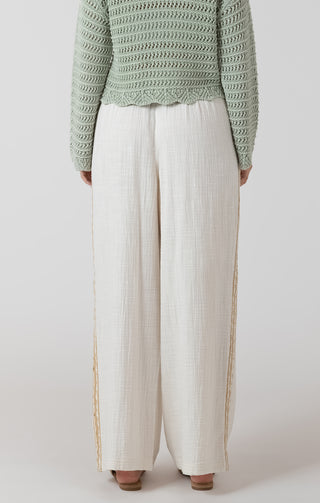 Person wearing a green textured sweater and white pants on a light gray background