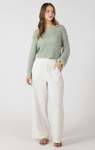 Woman wearing a green knitted sweater and white pants on a white background