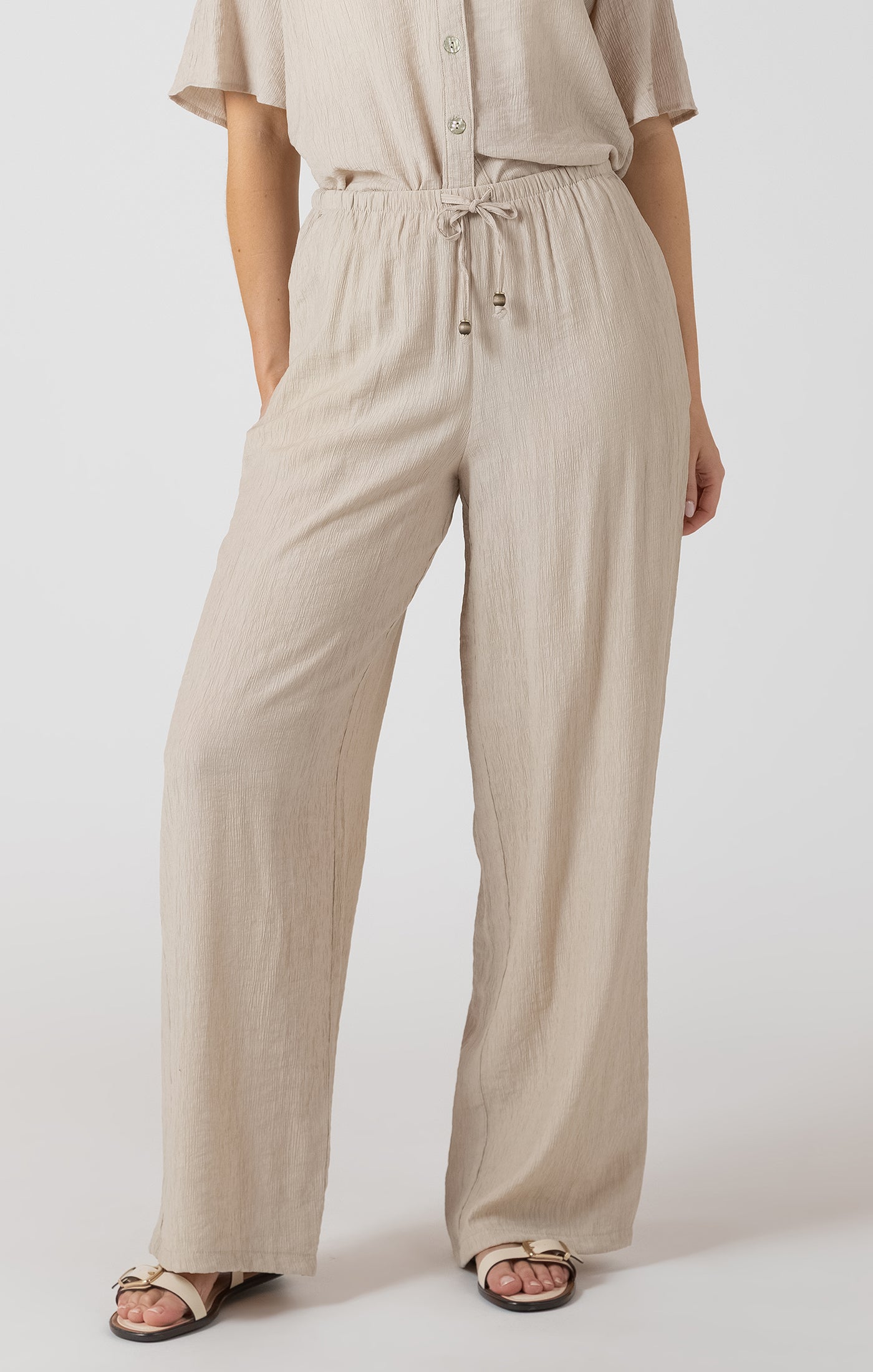 Person wearing a beige outfit with wide-leg pants on a white background