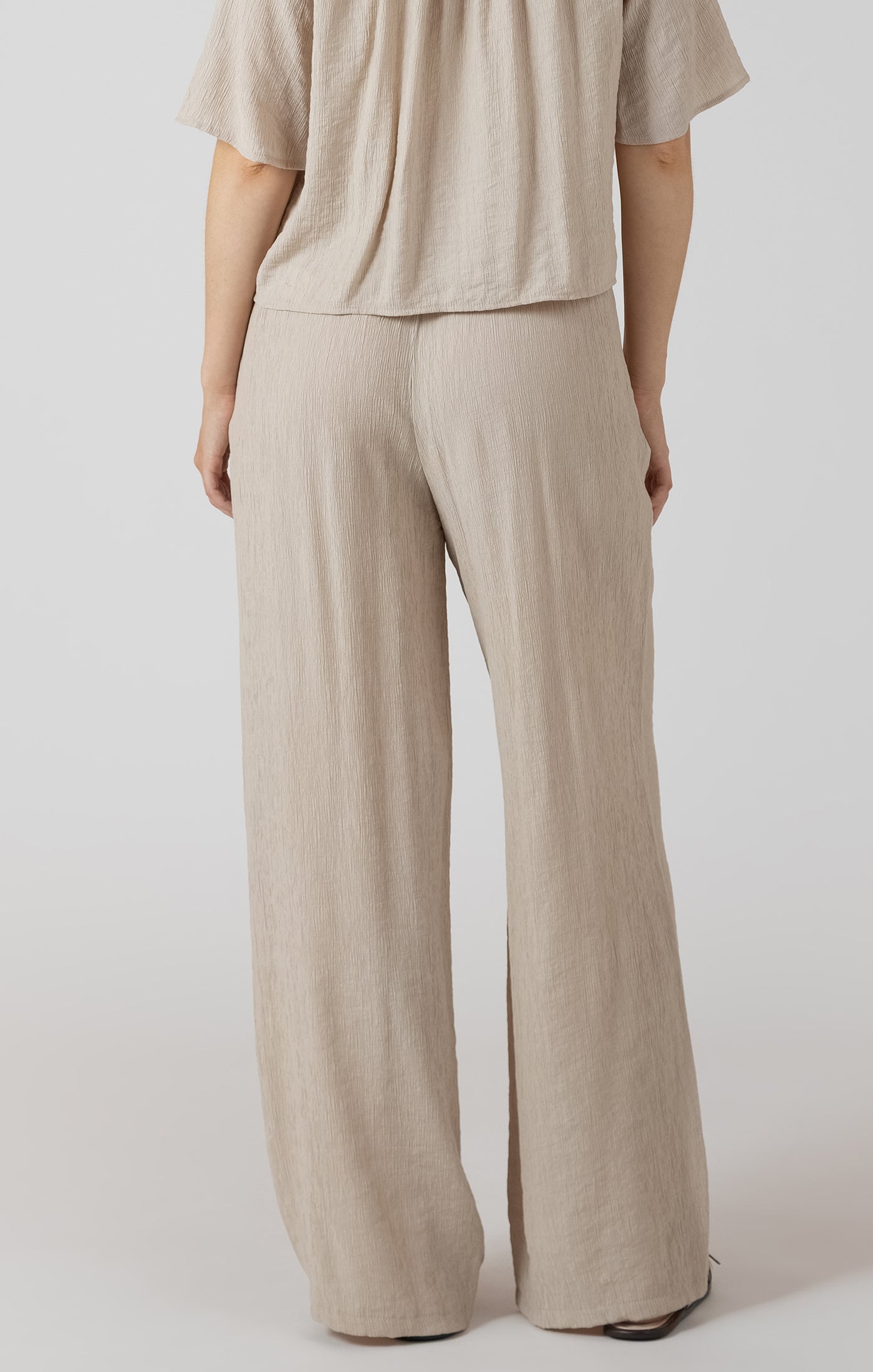 Person wearing beige pants and a matching top on a white background