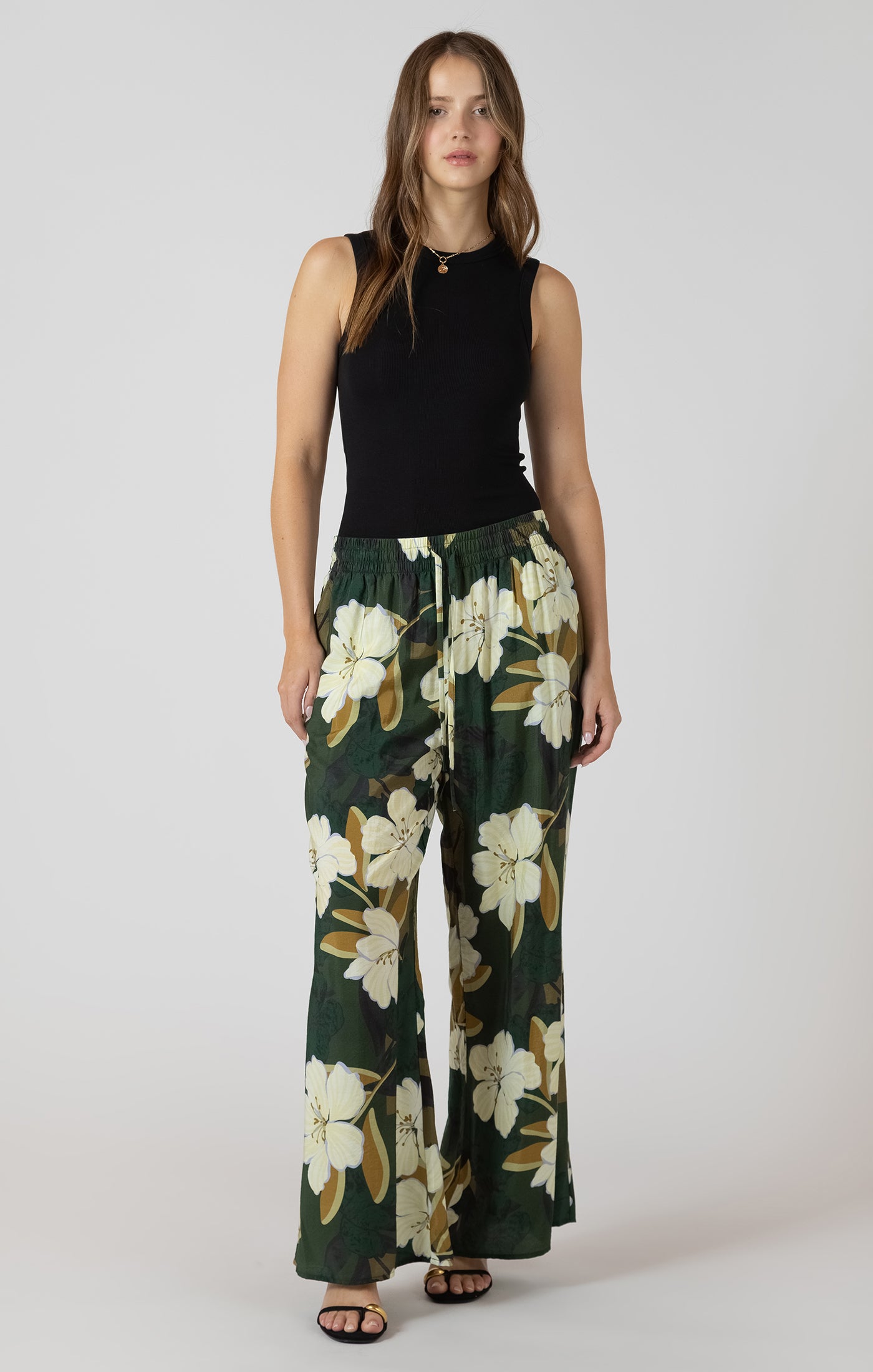 Woman wearing a black sleeveless top and floral wide-leg pants on a white background