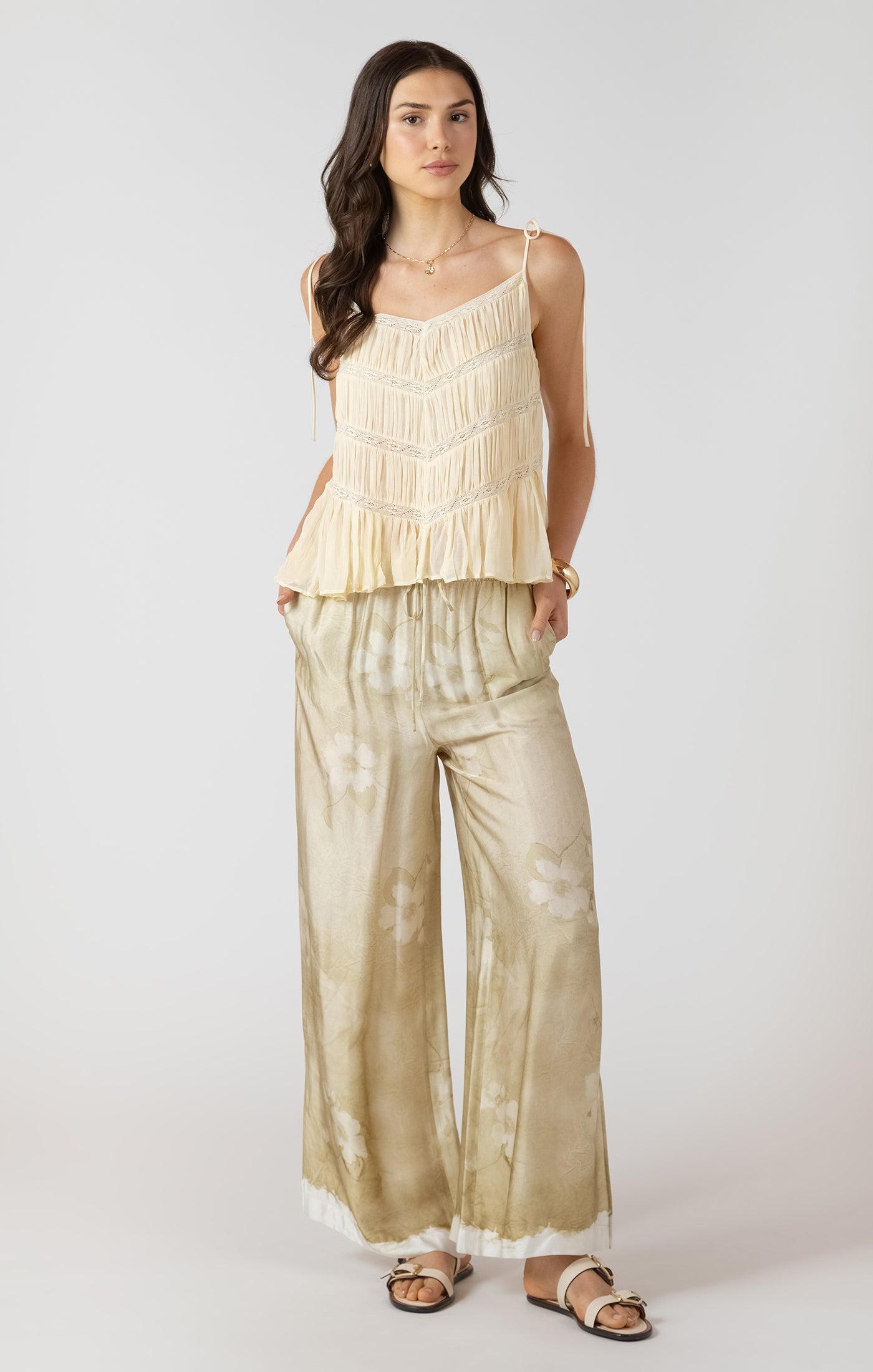 Woman wearing a beige ruffled top and wide-leg pants on a white background