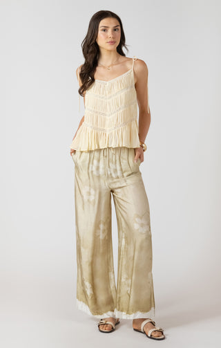 Woman wearing a beige ruffled top and wide-leg pants on a white background