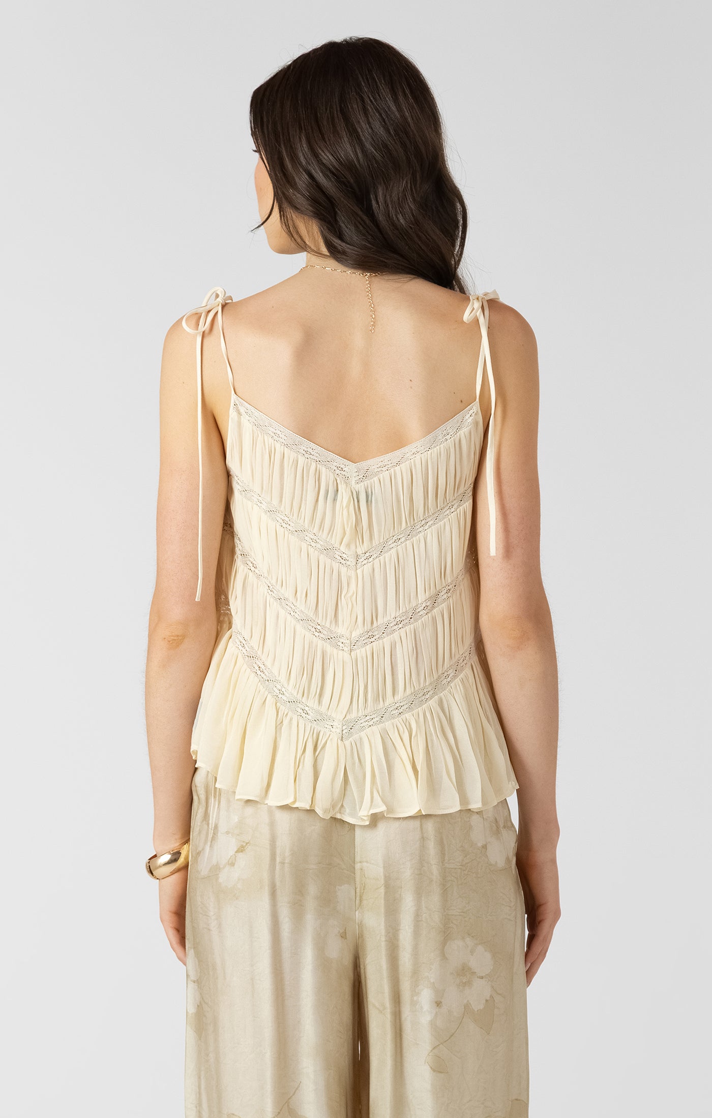 Woman wearing a beige sleeveless top with lace details on a plain background