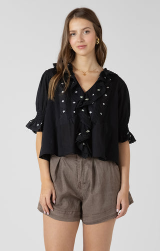 Women wearing a black blouse with white embroidered flowers on it. 
