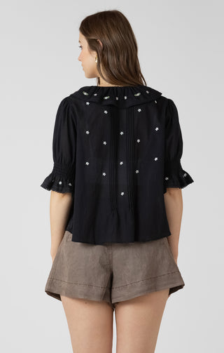 Women wearing a black blouse with white embroidered flowers on it. 