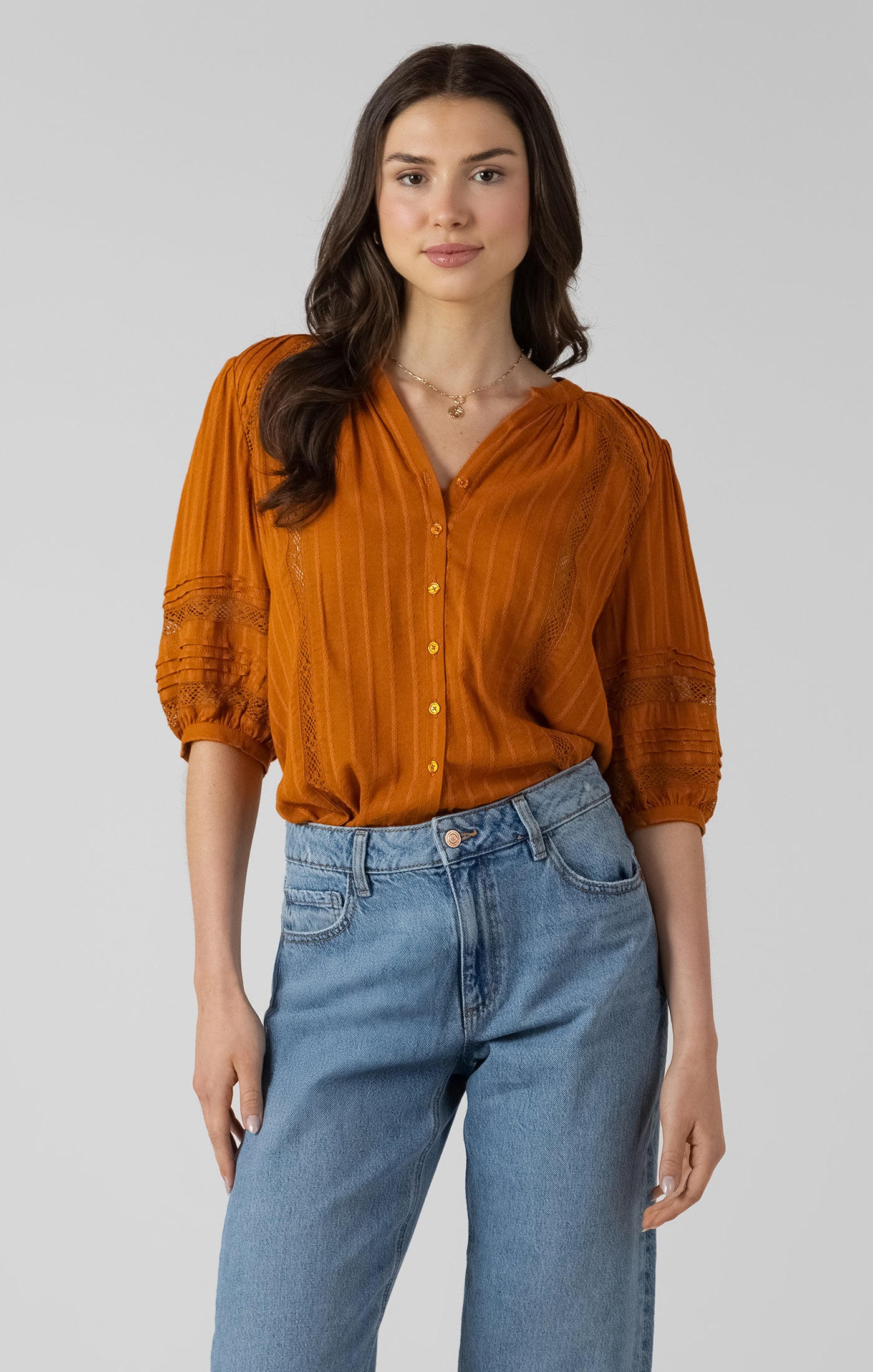 Woman wearing a rust-colored blouse and blue jeans on a plain background