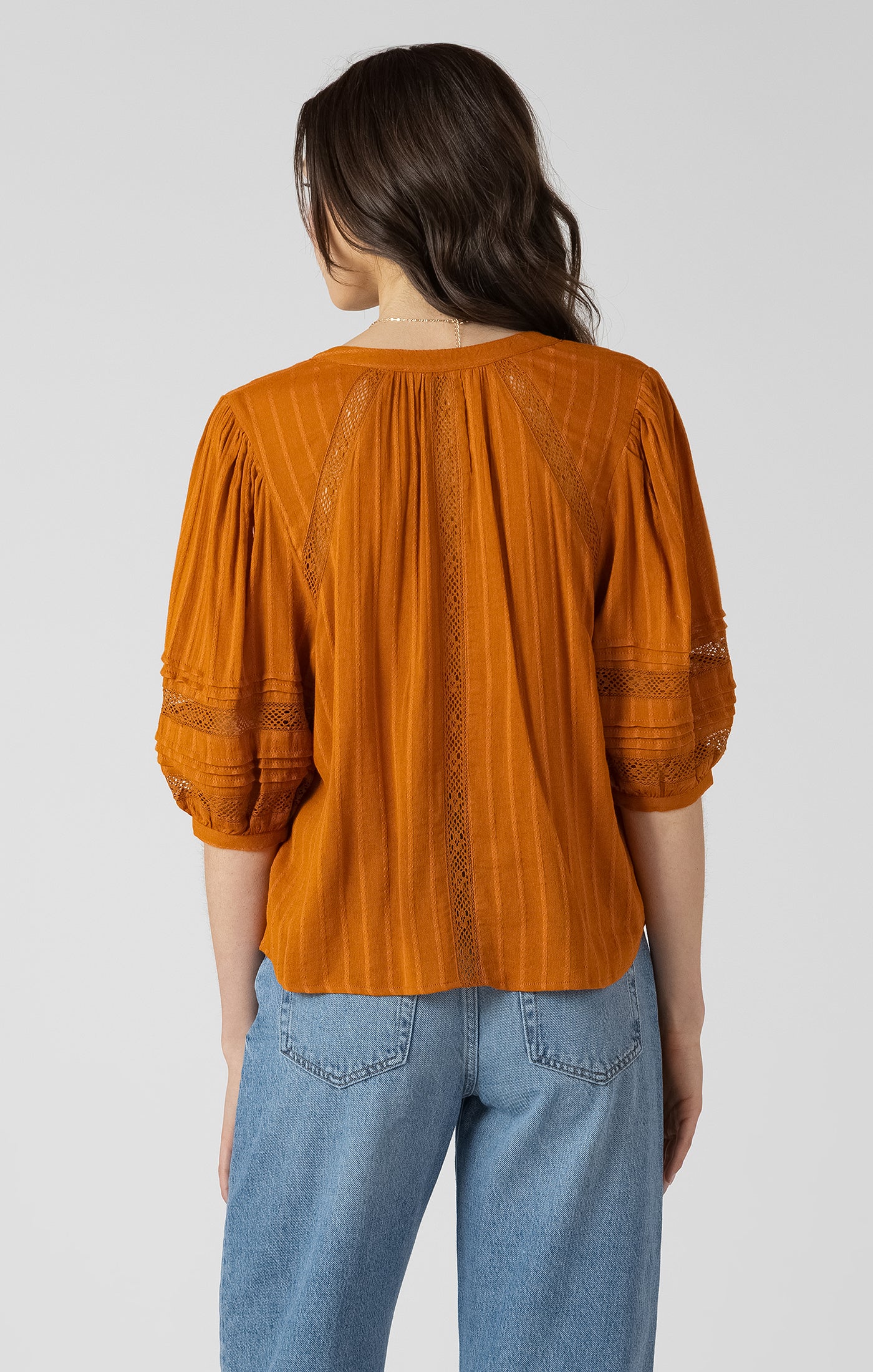 Woman wearing an orange blouse with lace details and blue jeans on a white background