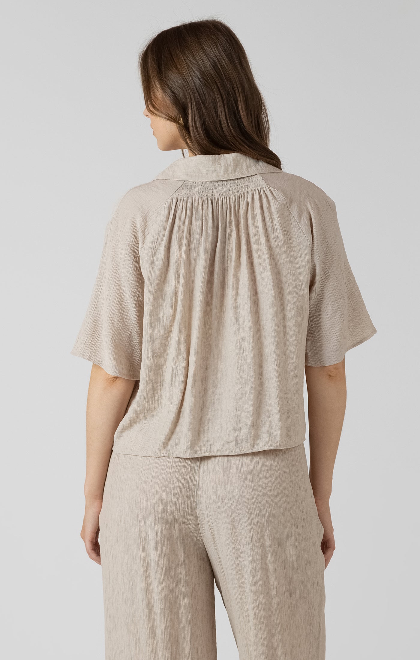 Woman wearing a beige short-sleeve top and pants on a light gray background