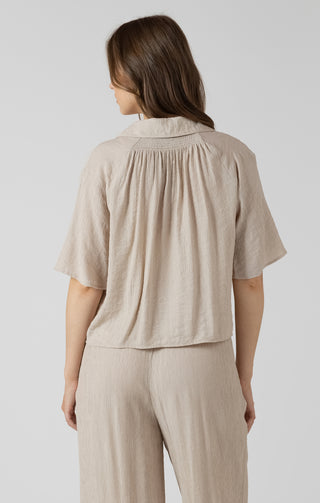 Woman wearing a beige short-sleeve top and pants on a light gray background