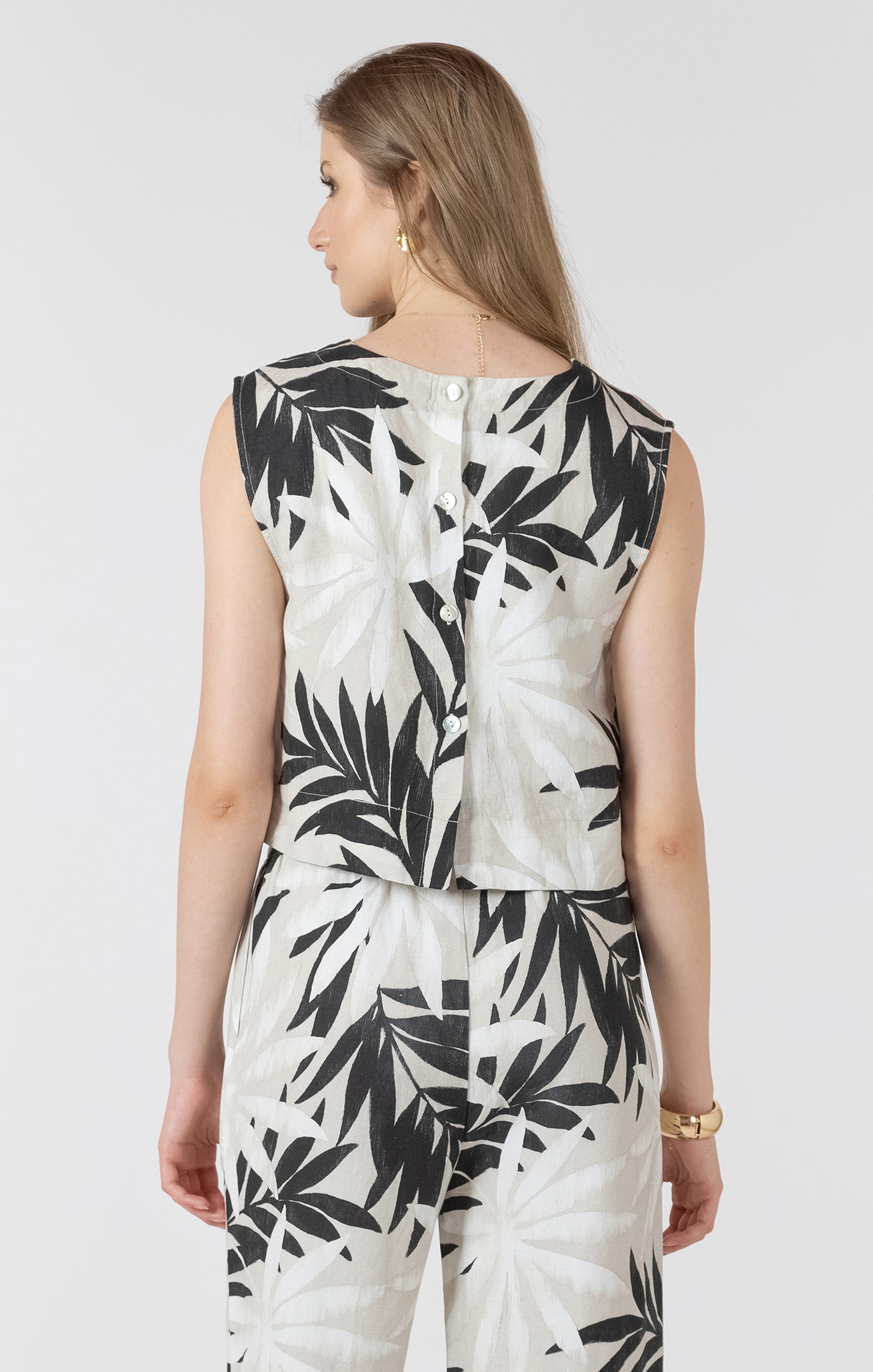 Woman wearing a white outfit with black leaf pattern on a plain background