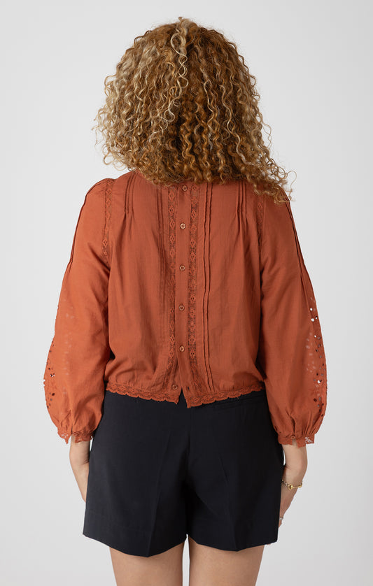 Person wearing a rust-colored blouse and black shorts on a white background