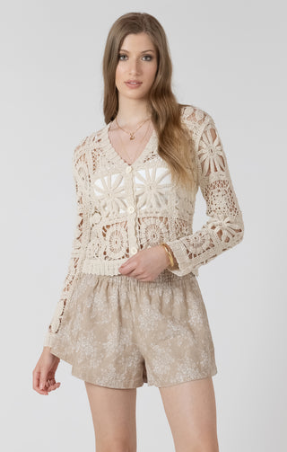 Woman wearing a beige crochet top and shorts on a white background