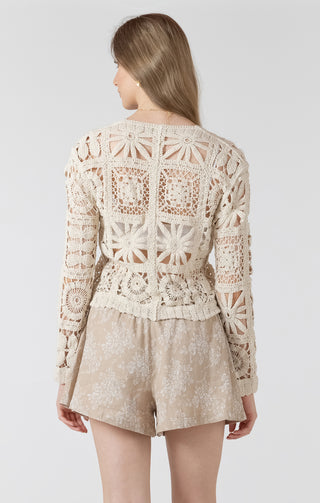 Woman wearing a beige crochet top and shorts on a white background