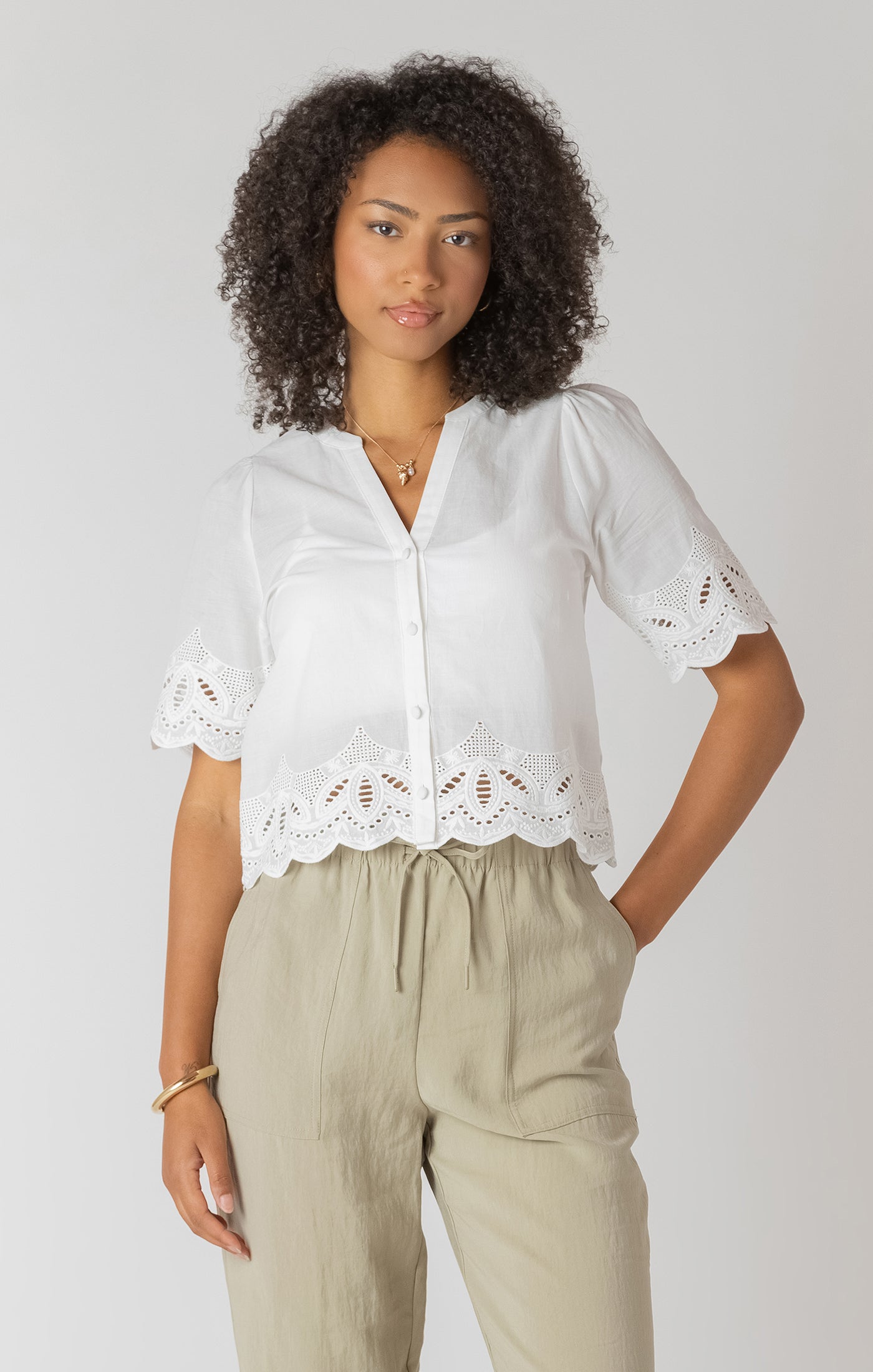 Woman wearing a white blouse with lace details and beige pants on a plain background