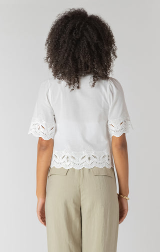 Person wearing a white blouse with lace details and beige pants on a plain background