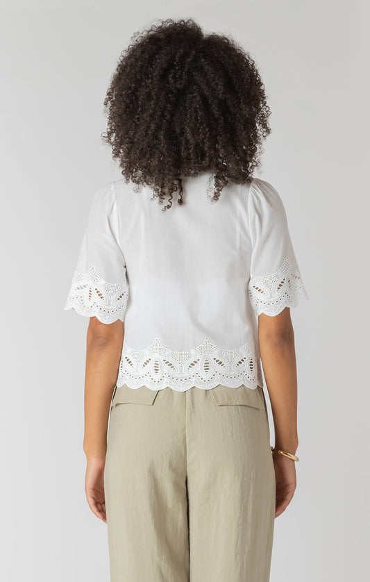 Person wearing a white blouse with lace details and beige pants on a plain background