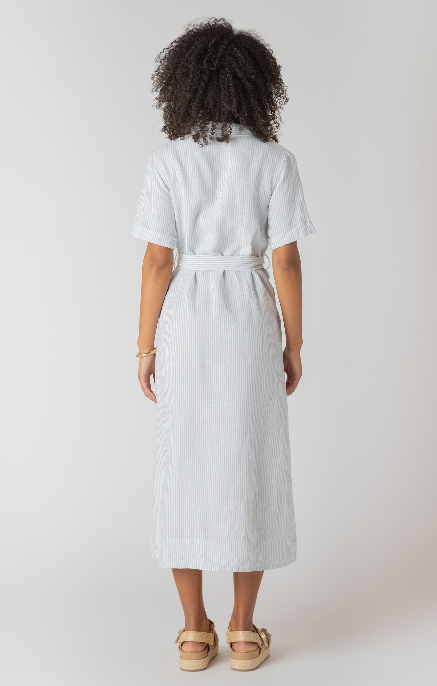 Person wearing a white and blue stripe dress with a belt on a plain background
