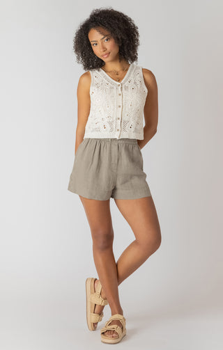 Woman wearing a white sleeveless top and beige shorts on a plain background