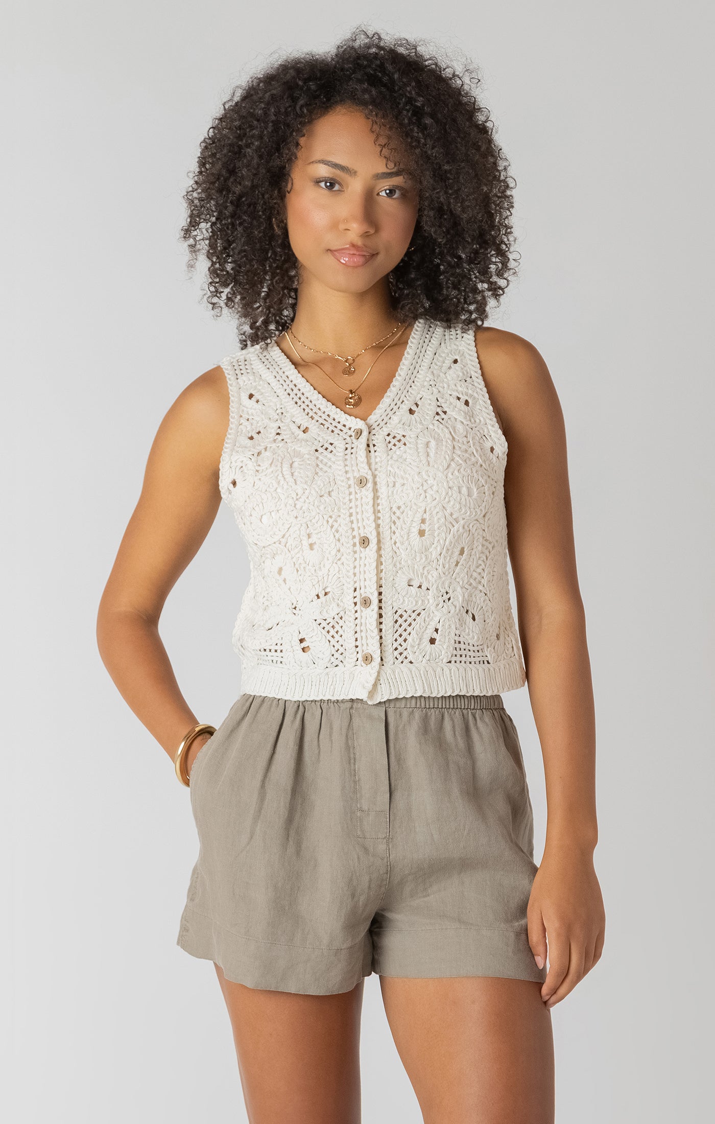 Woman wearing a white lace top and beige shorts on a plain background