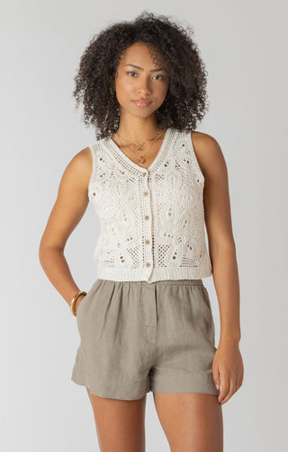 Woman wearing a white lace top and beige shorts on a plain background